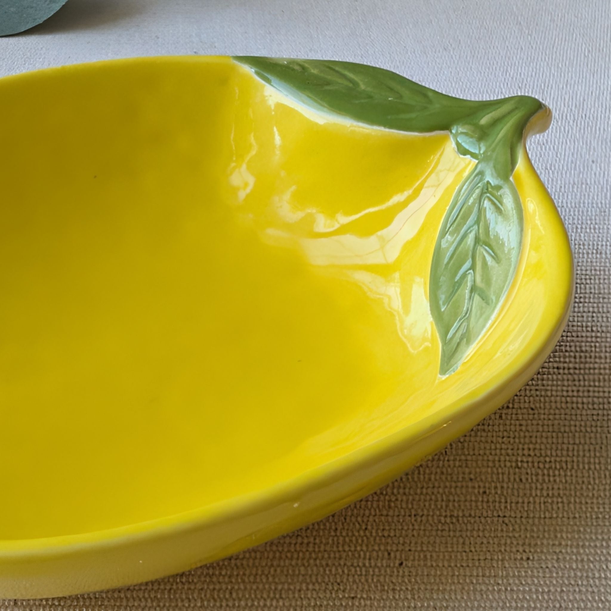 Lemon-shaped yellow ceramic plate with glossy finish and green leaf detail