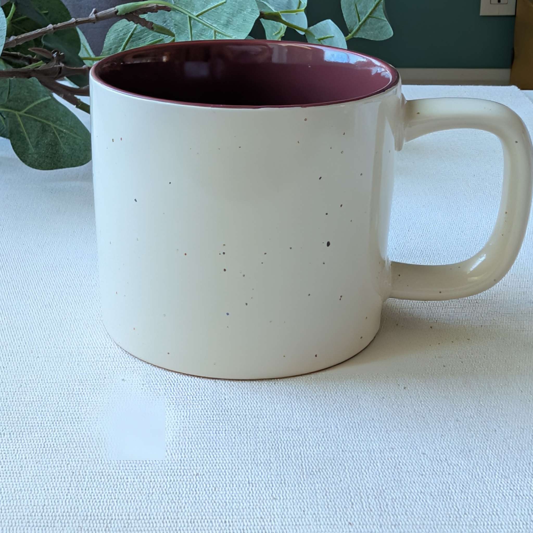 Speckled ceramic mug with a removable burgundy knit sleeve and button detail