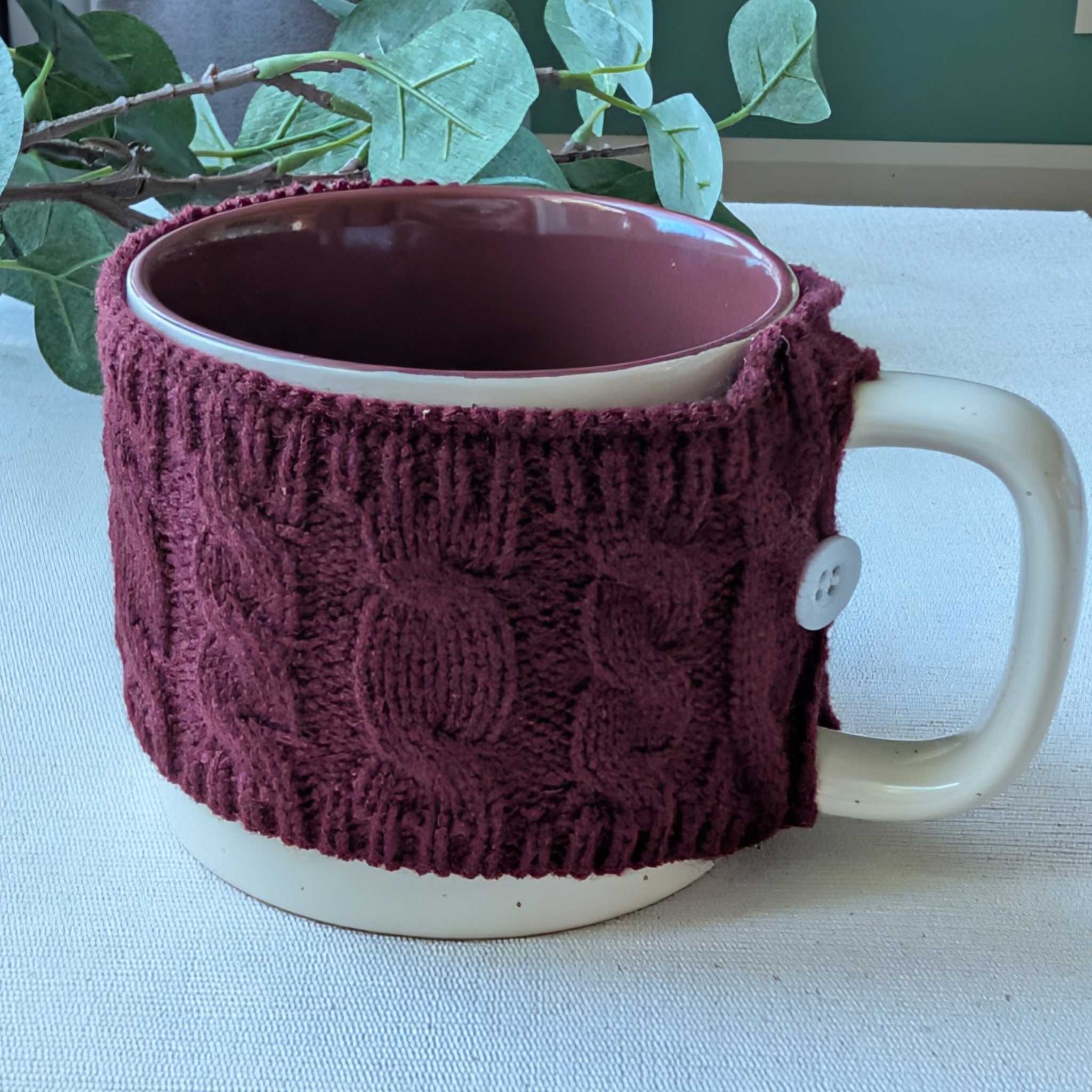 Speckled ceramic mug with a removable burgundy knit sleeve and button detail